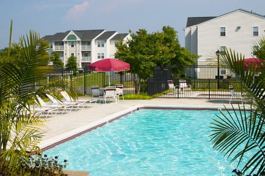 Fenced in pool with sun chairs, patio table with umbrella and seating