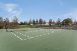 Exterior Acclaim at Sterling tennis courts, Autumn foliage in the distance, neutral toned buildings in the background, photo taken on a sunny day.