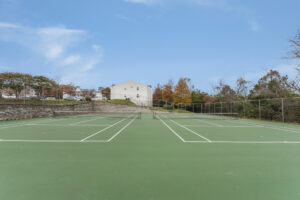 Exterior Acclaim at Sterling tennis courts, Autumn foliage in the distance, neutral toned buildings in the background, photo taken on a sunny day.