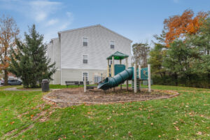 Exterior Acclaim at Sterling Playground, soft landing ground, wood perimeter, autumn foliage in background, neutral toned building, meticulous landscaping, photo taken on a sunny day.
