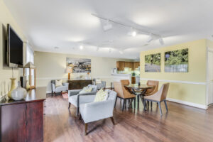 Interior Acclaim at Sterling lobby, wood floors, rustic decor, circular table with four seats, lounge chairs, community kitchen in back of room, nature photographs on walls, overhead lighting, yellow walls.