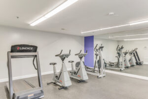 Interior Fitness Center, padded floor, mirrored wall, elliptical machine, two stationary bikes, treadmill.